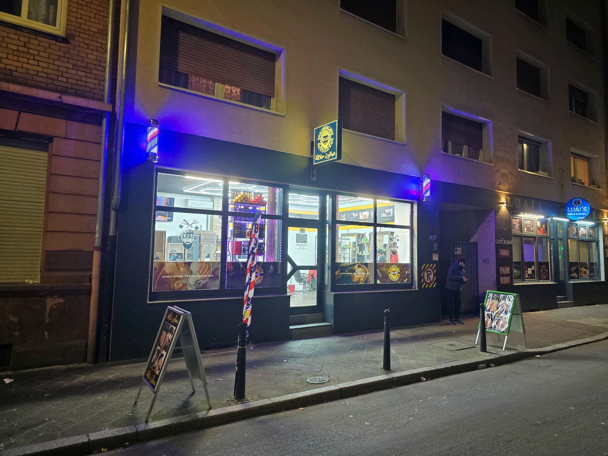 Ladenfront von DELUX in J2, 16 am Abend, mit beleuchteten Barber-Poles